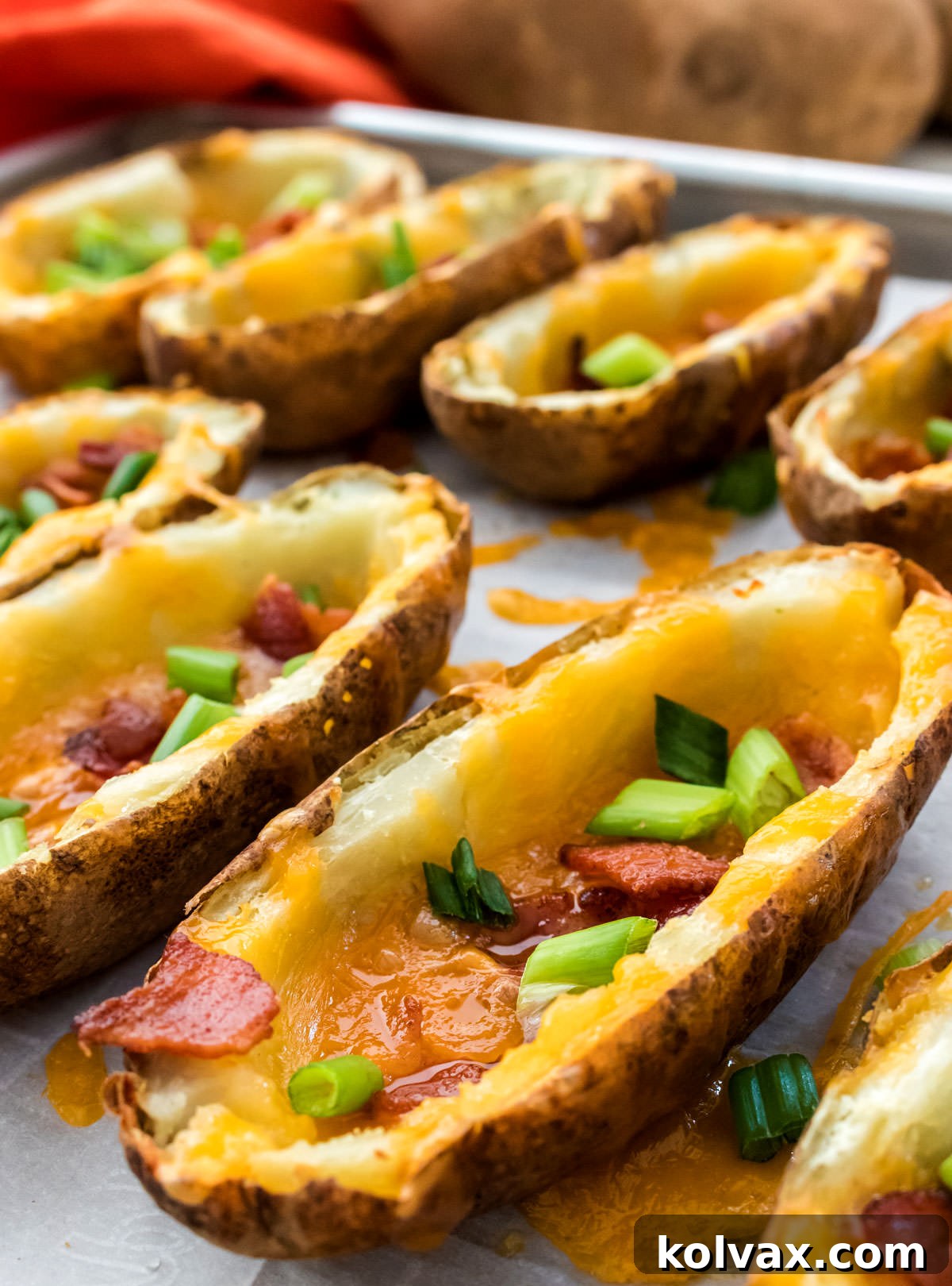 Crispy Loaded Potato Boats 5 Closeup on eight freshly baked Potato Skins, golden brown and bubbling with melted cheese and crispy bacon, straight out of the oven on a parchment-lined cookie sheet.