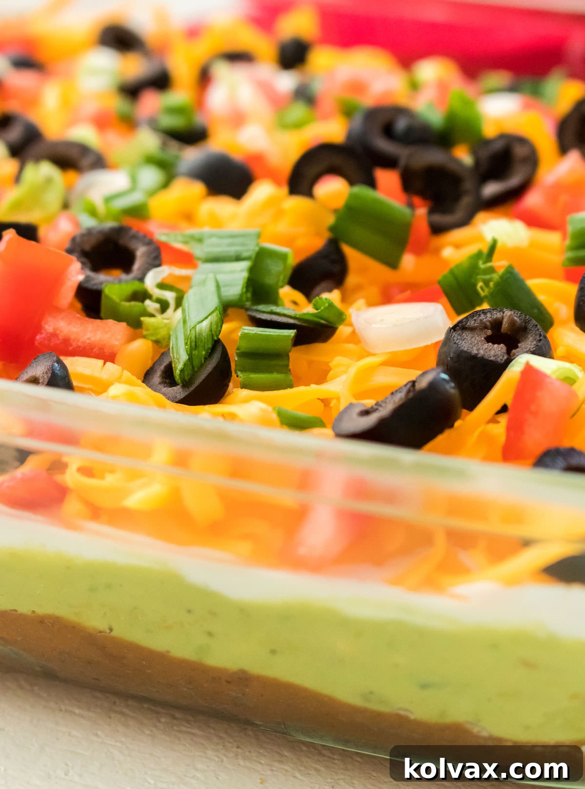 A full 9x13" clear glass baking dish filled with an exquisite 7 Layer Dip, perfectly centered on a clean white table, ready to be served. The layers are vibrant and appealing, promising a delicious party treat.