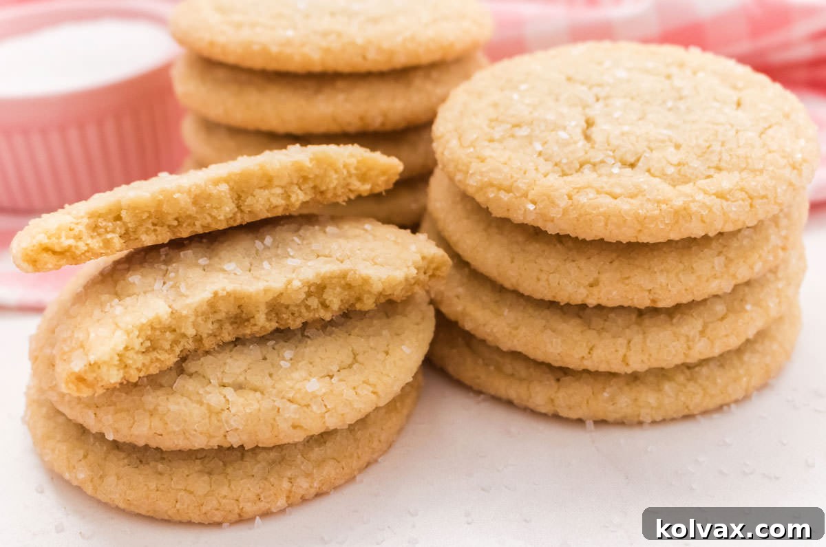 Close up on three stacks of Soft and Chewy Sugar Cookies sitting on a white surface in front of a pink plaid table linen.