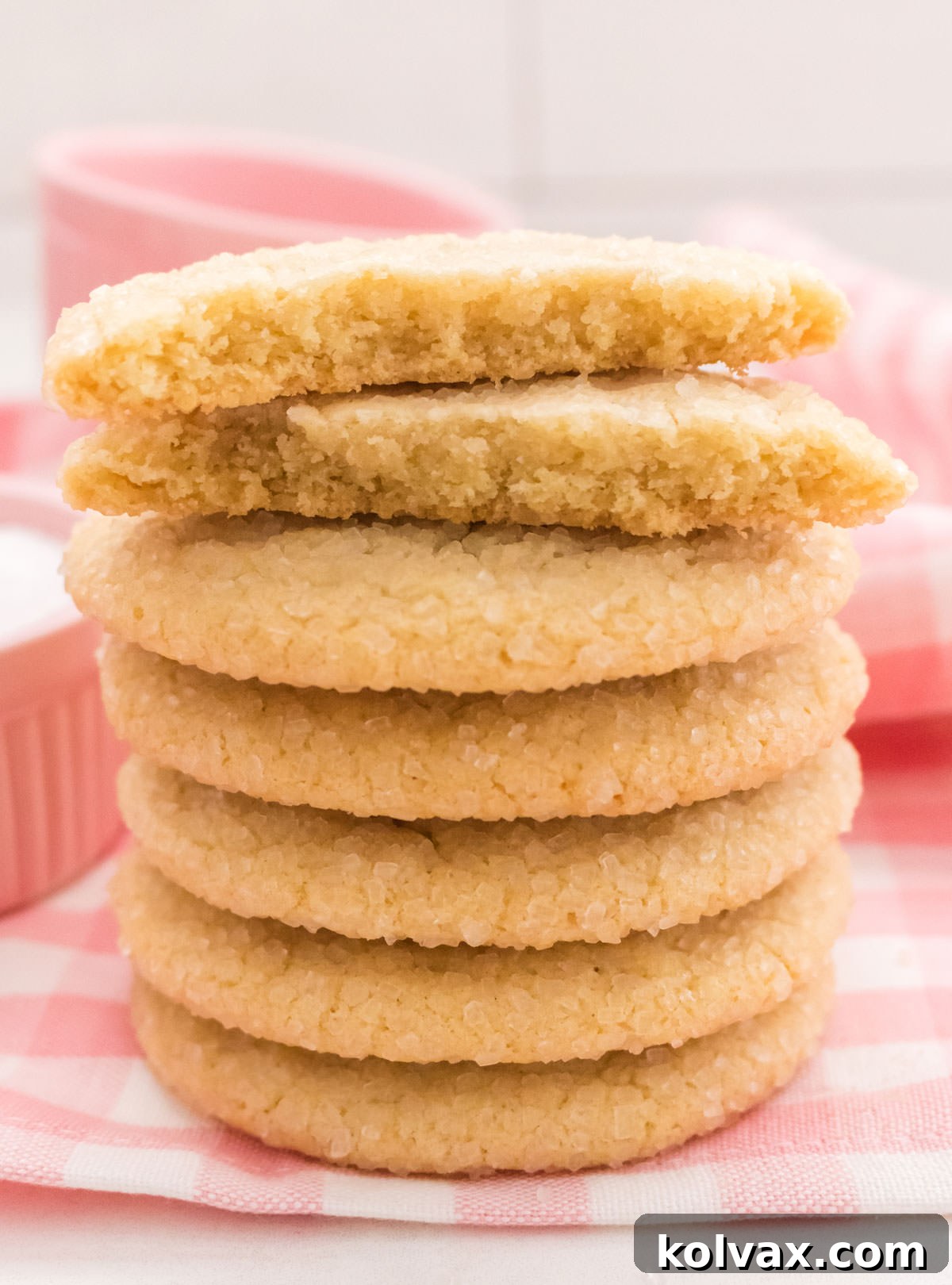 Closeup on a tall stack of Soft and Chewy Sugar Cookies sitting on a pink plain table linen with the top cookie split in half.