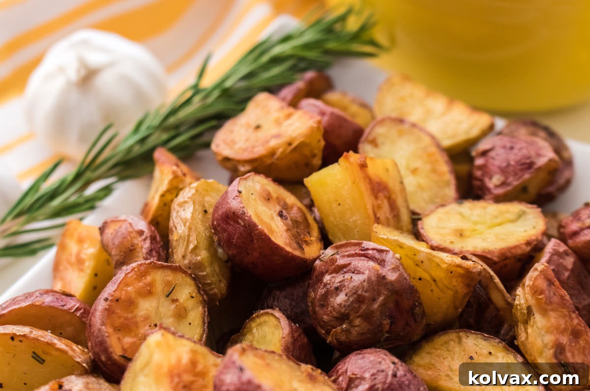Closeup on a white serving platter filled with Crispy Garlic Roasted Potatoes with a head of garlic and a sprig of rosemary off to the side.