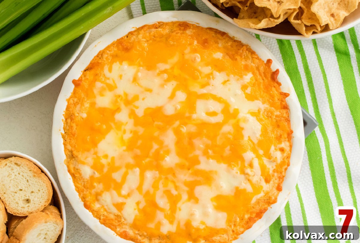 An overhead shot of a white ceramic baking dish containing the prepared Buffalo Chicken Dip, generously covered with an even layer of shredded cheese, perfectly poised and ready to be baked to golden, bubbly perfection.