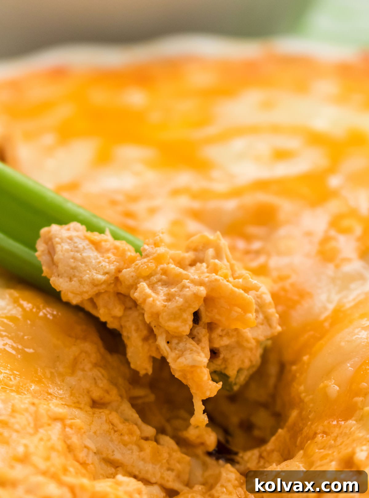 A close-up view of a serving platter featuring a luscious Buffalo Chicken Dip, rich with melted cheese and ready to be enjoyed, with a crisp celery stick poised to scoop up a delicious bite.
