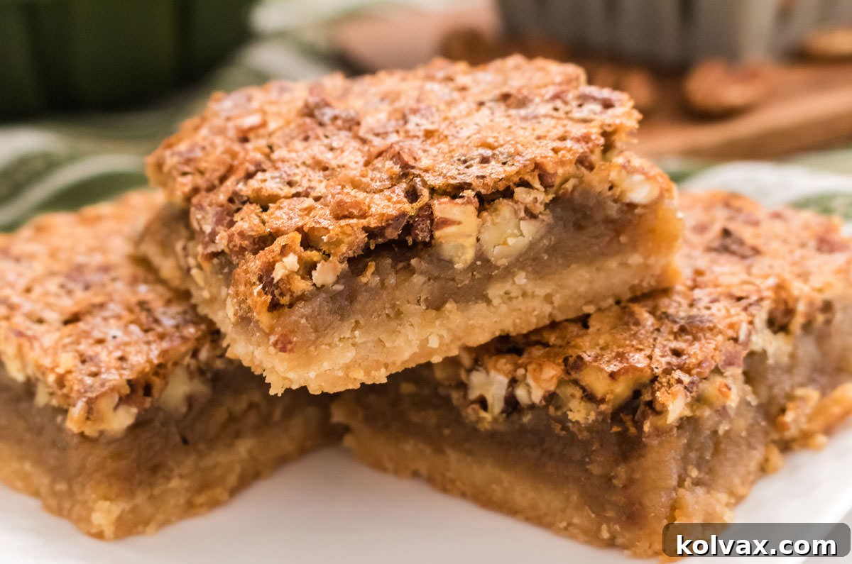 Closeup on a stack of three Pecan Pie Bars sitting on a white plate, showcasing their inviting texture and golden-brown hue, ready to be enjoyed.