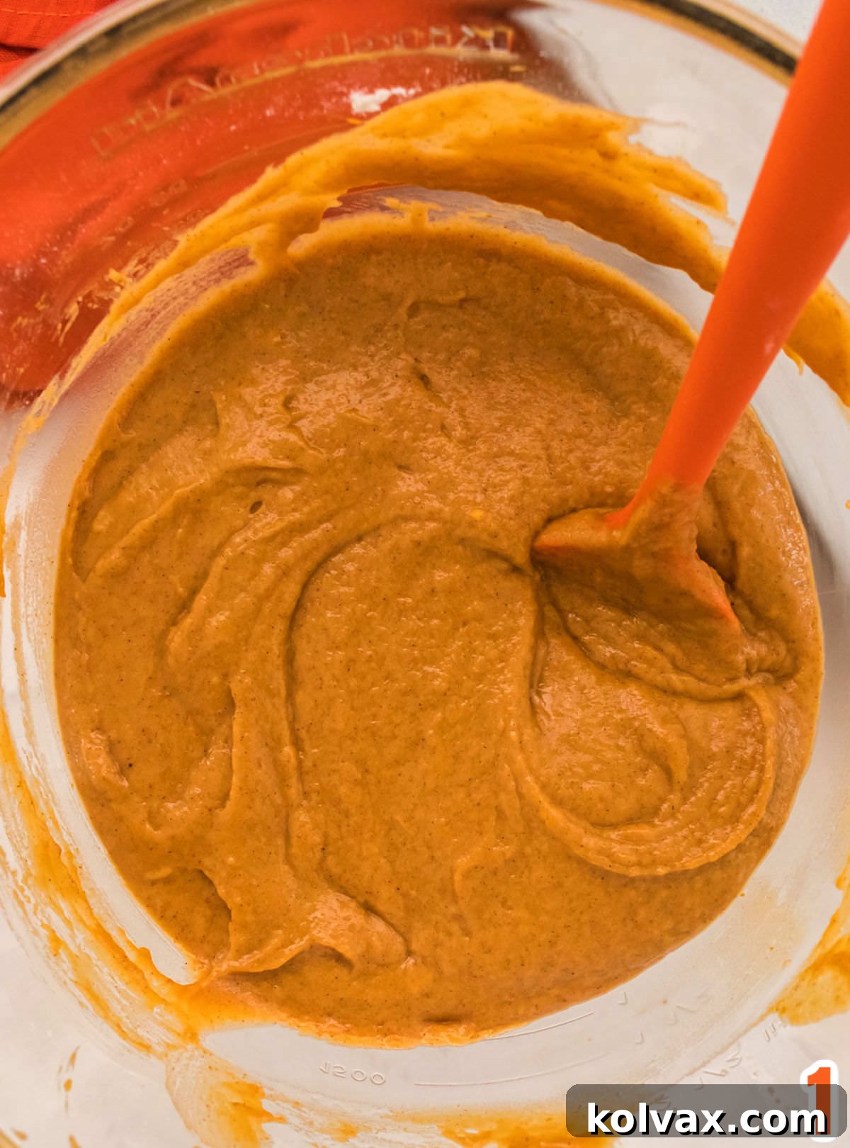 Closeup on a bowl of Pumpkin Bar batter in a glass bowl with a orange spoon.