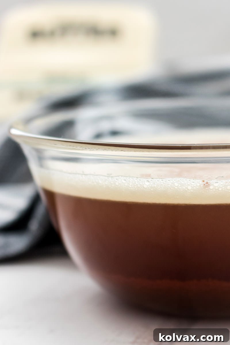 A glistening bowl of perfectly browned butter, with a fresh stick of butter visible in the background, illustrating the transformation and readiness for use.