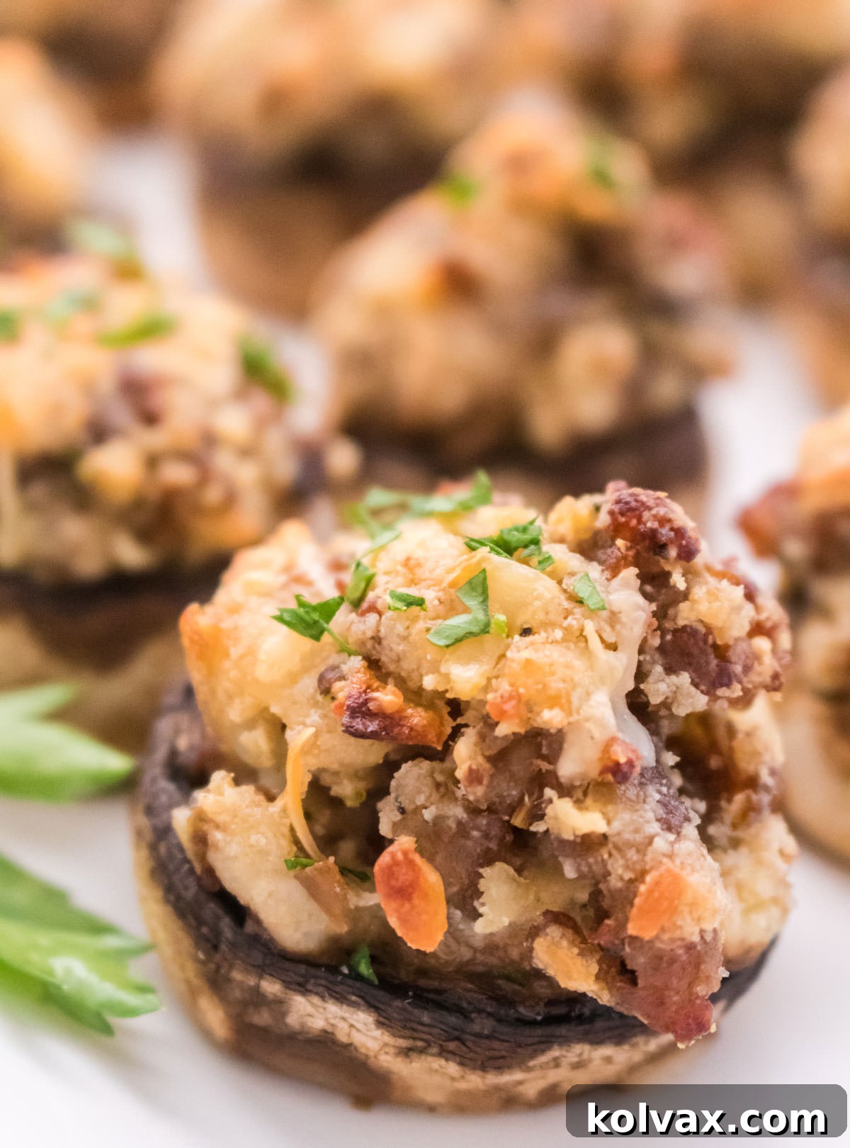 Closeup on a freshly baked, golden brown Stuffed Mushroom appetizer, perfectly garnished and presented on a white serving platter.