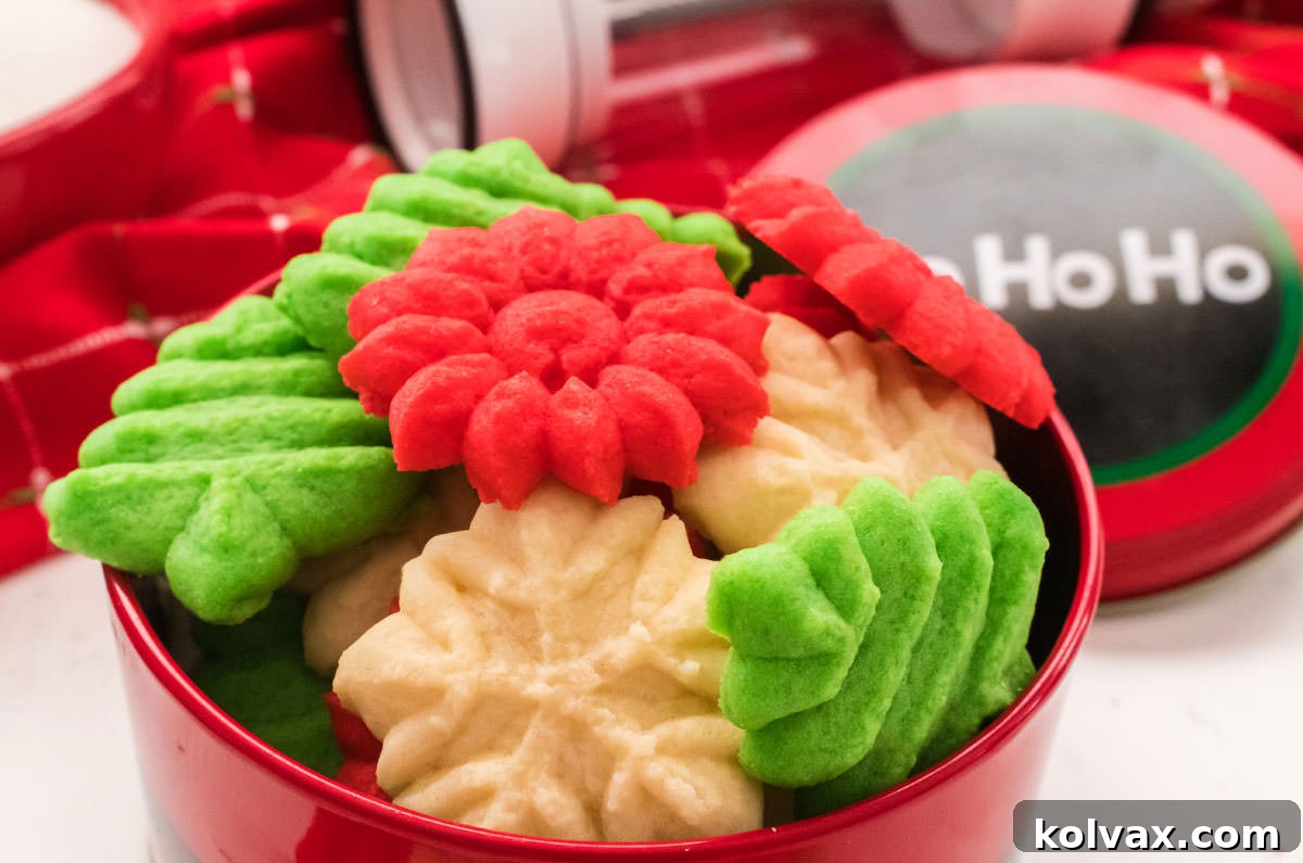 A festive tin filled with red, white, and green Classic Spritz Cookies, showcasing their delicate shapes perfect for Christmas celebrations.