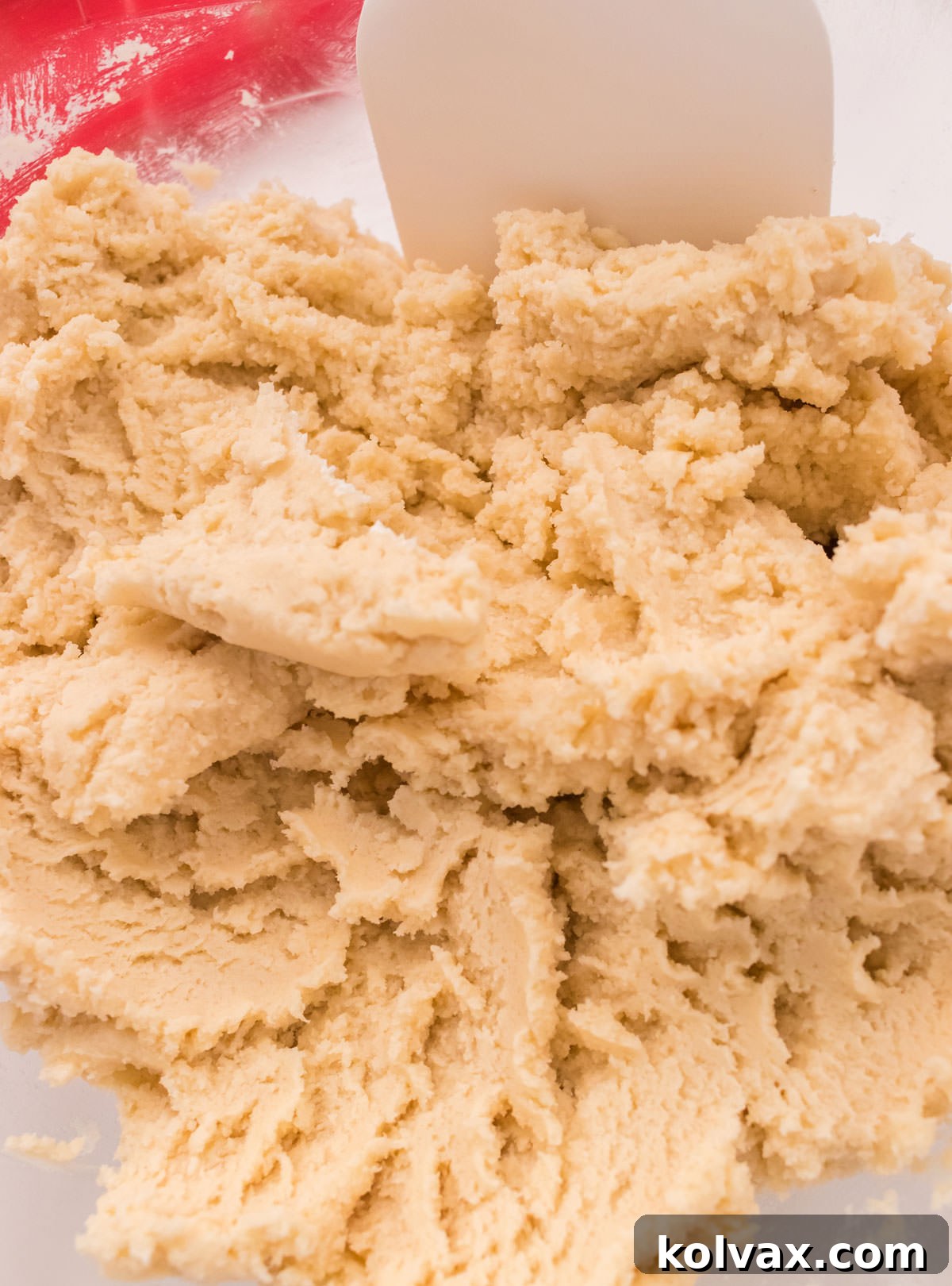 Close-up view of the smooth, pale yellow Spritz Cookie dough in a clear mixing bowl, ready for coloring.