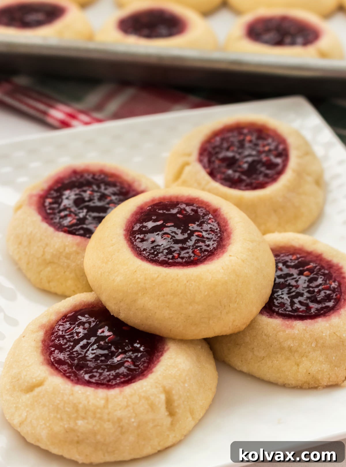 Five Thumbprint Cookies sitting on a white plate with a Christmas towel in the background.