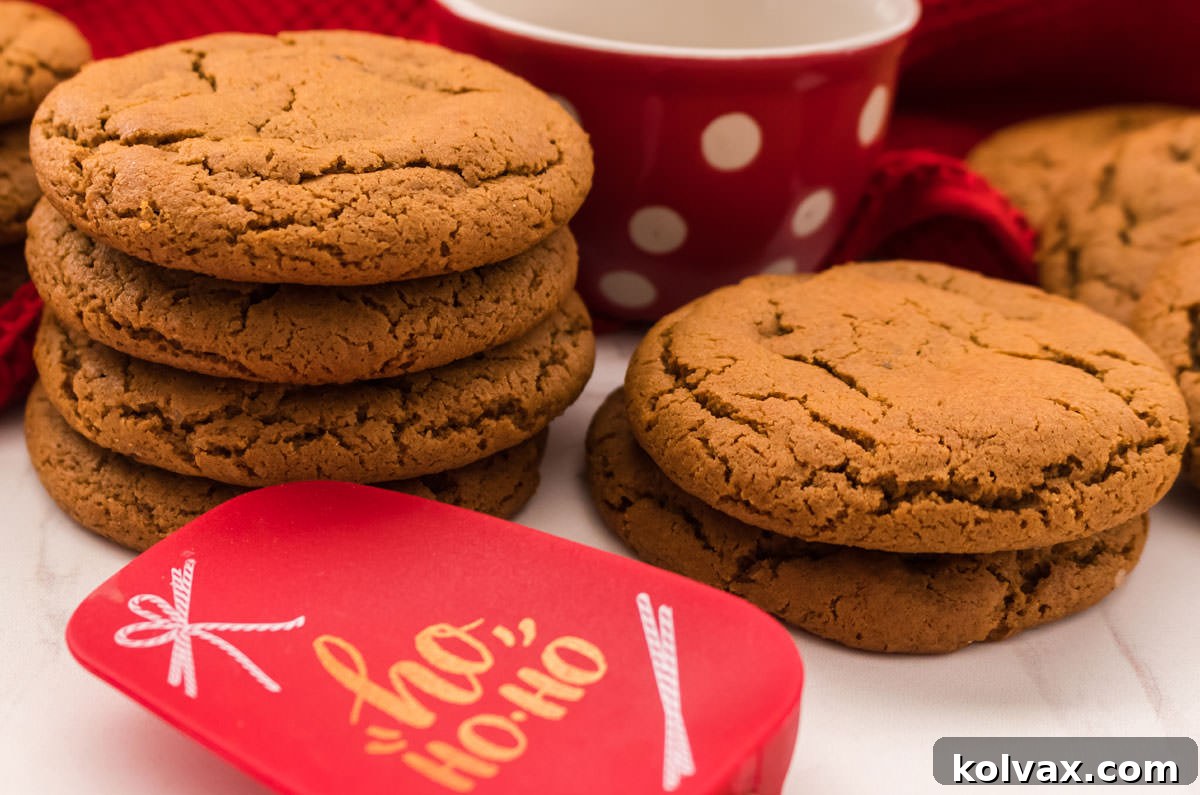 Two stacks of glistening Soft Molasses Cookies, perfectly baked, placed in front of a festive Christmas coffee mug. A Christmas-themed spatula rests in the foreground, hinting at holiday baking and cozy moments.