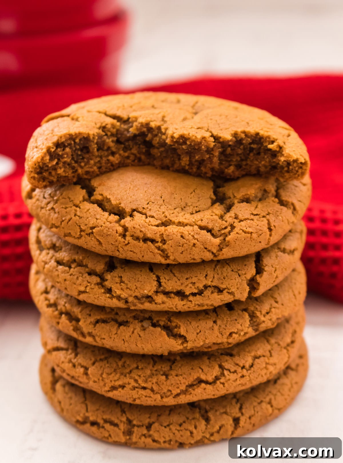 A tempting stack of Soft Molasses Cookies nestled on a rustic white wooden board, with a festive red Christmas kitchen towel artfully blurred in the background, creating a cozy holiday scene.