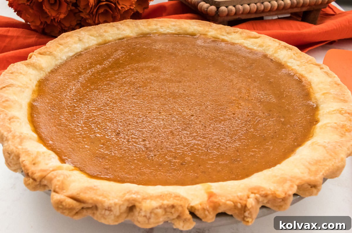 A beautifully baked Homemade Sweet Potato Pie, golden-brown and inviting, resting on a pristine white board with a soft orange linen draped elegantly in the background. The pie boasts a perfect crust and a smooth, inviting filling, promising a delightful culinary experience.