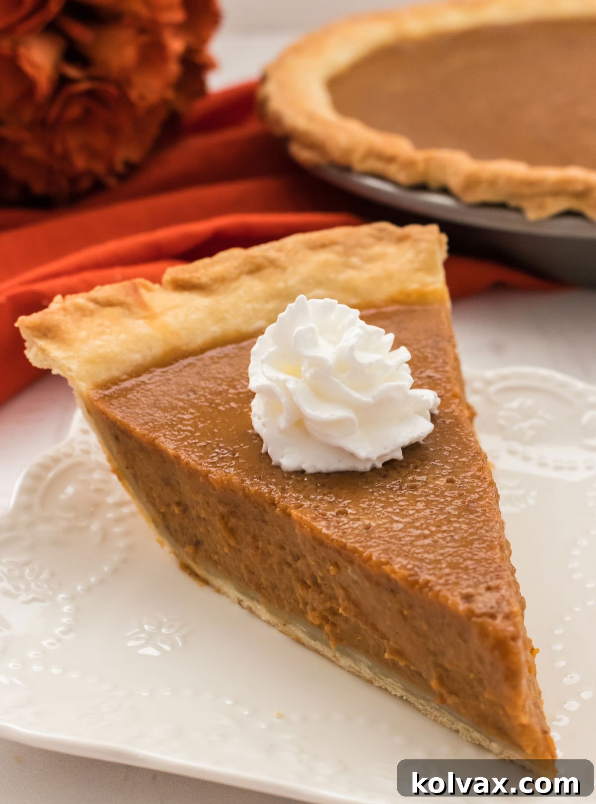A slice of Homemade Sweet Potato Pie, elegantly presented on a white plate, crowned with a generous dollop of fluffy whipped cream, inviting you to take a bite.