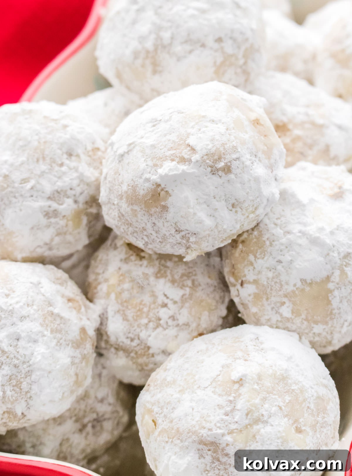 A large number of Snowball Cookies stacked high in a red Christmas ceramic container, evoking a festive and abundant feel.