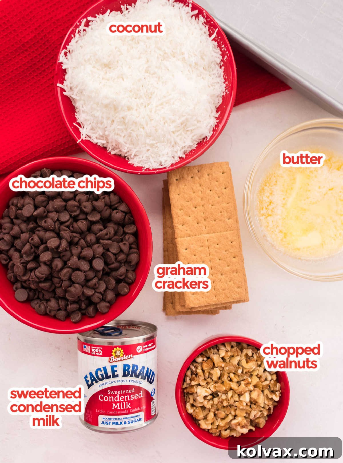 All the core ingredients for Magic Bars laid out: Graham Crackers, Chocolate Chips, Shredded Coconut, Butter, Chopped Walnuts, and Sweetened Condensed Milk.