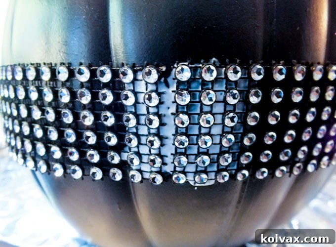 Adding rhinestone ribbon to a black pumpkin for decoration