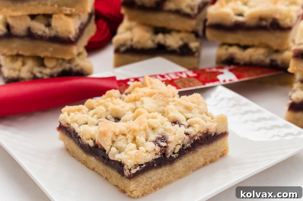 A slice of Shortbread Cookie Bar with a vibrant red jam layer, resting on a white plate with a festive Christmas knife in the background, hinting at holiday baking.