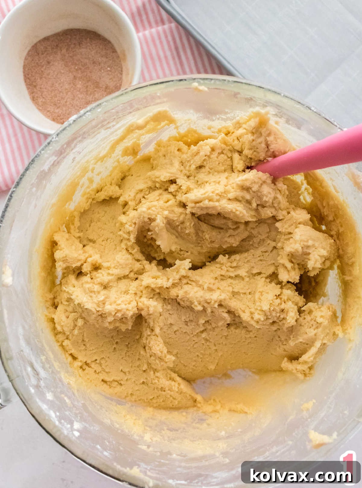 Snickerdoodle cookie dough in a clear glass bowl on a white table.