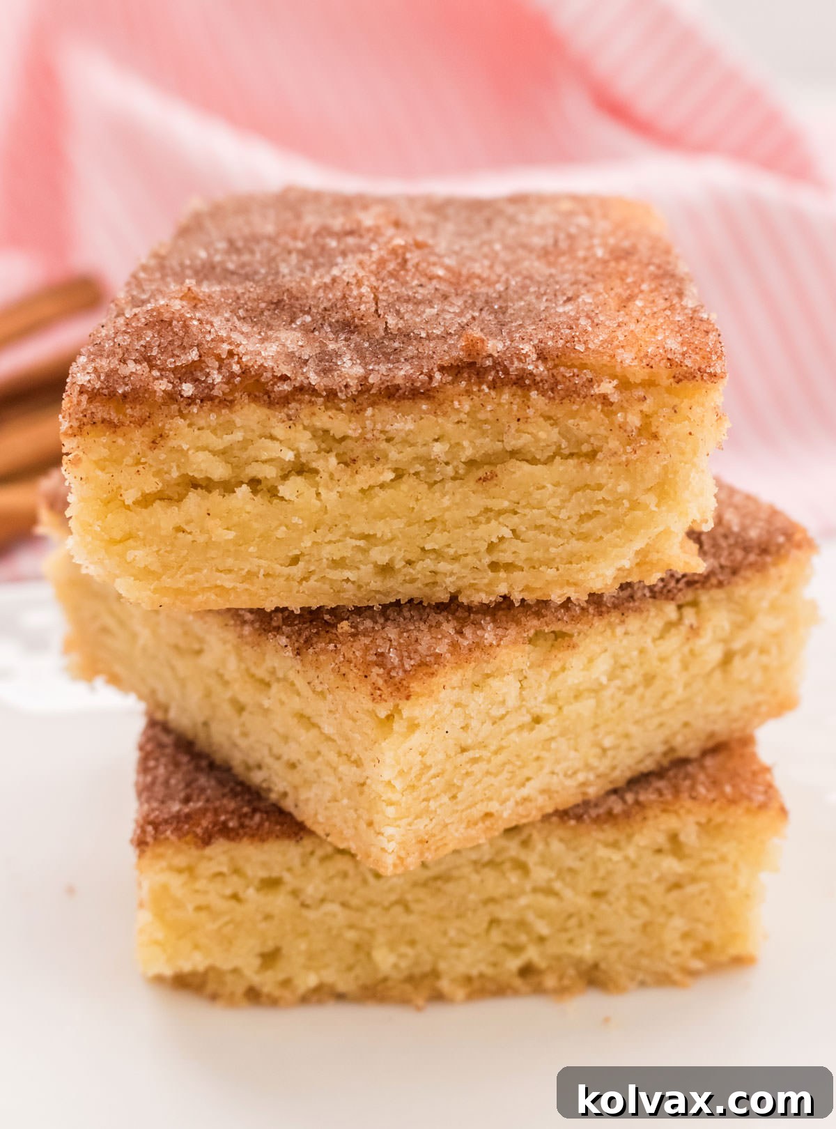 Stack of three Snickerdoodle Bars on a white surface with a pink kitchen towel in the back.