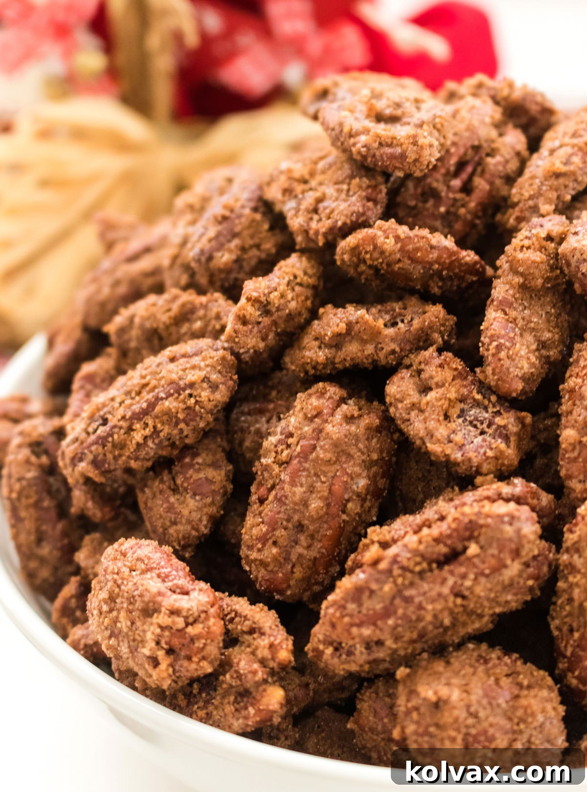 A close up of a bowl of freshly baked Candied Pecans in a white bowl, showing their golden brown, crunchy coating.