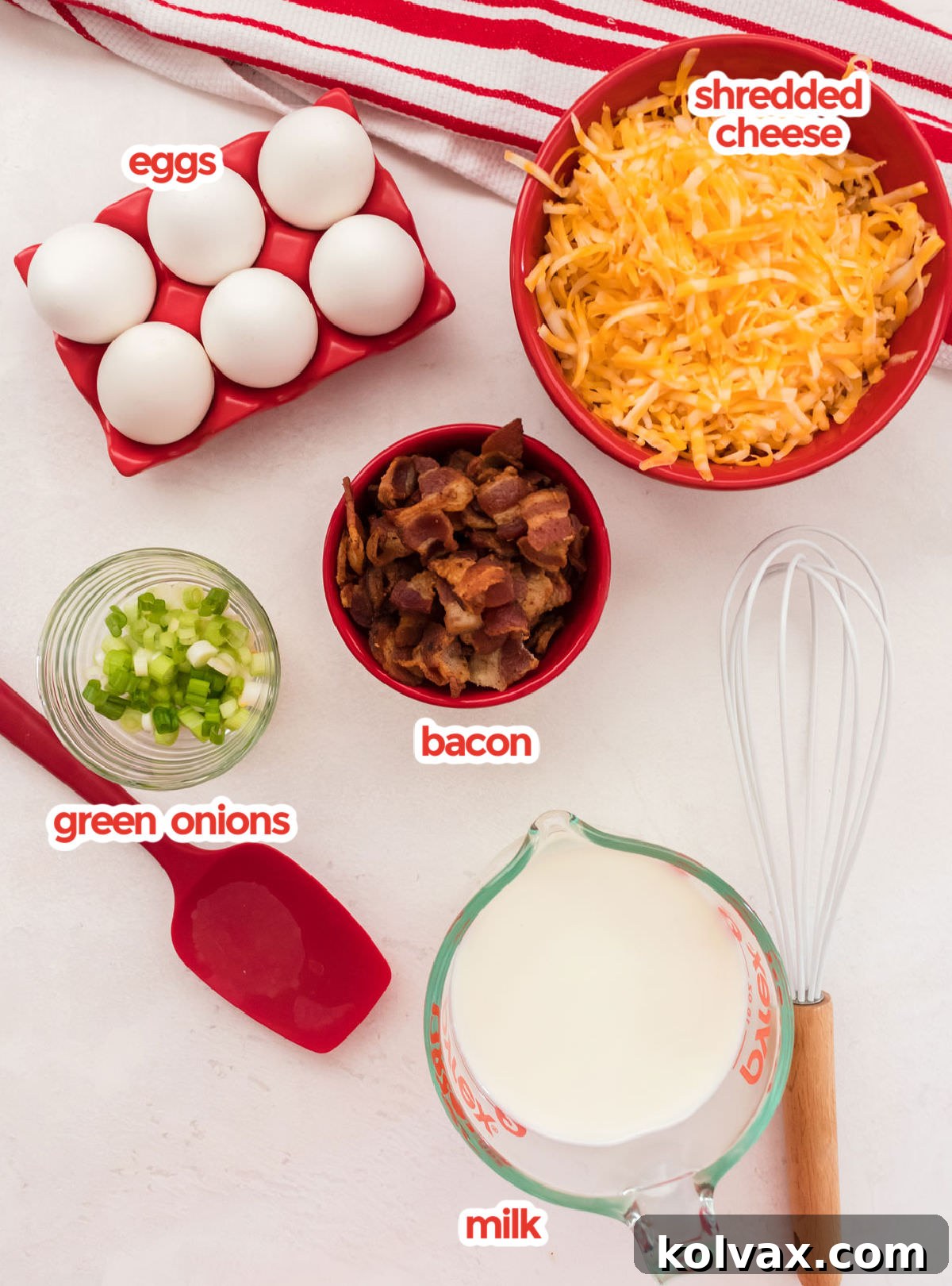 A beautifully arranged selection of fresh ingredients required to make Quiche Lorraine, including farm-fresh eggs, various cheeses, vibrant green onions, crispy cooked bacon, and a carton of milk.