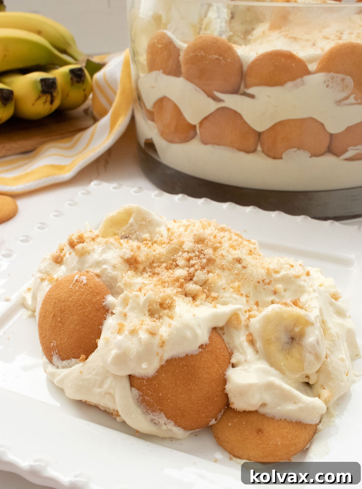 A perfectly portioned serving of banana pudding on a white plate, positioned in front of the large, assembled bowl of pudding, ready to be enjoyed.