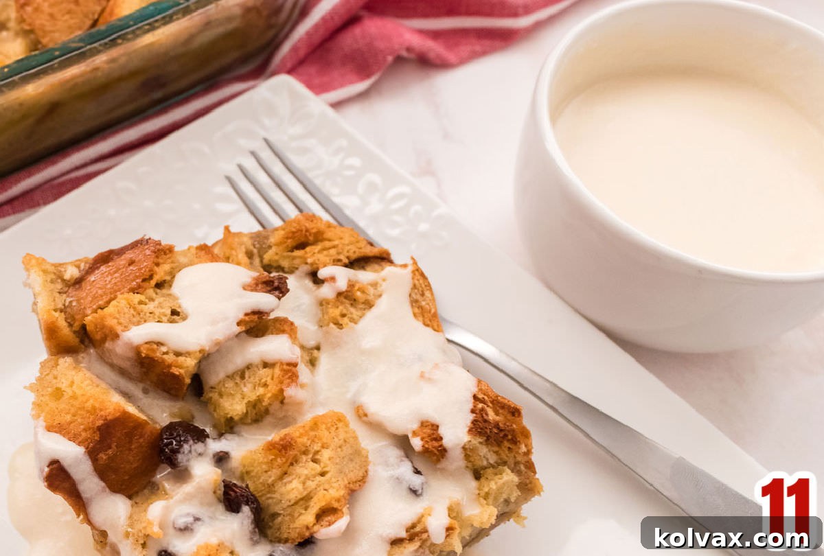 A small white bowl of creamy vanilla sauce placed beside a generous slice of warm bread pudding on a white plate, ready to be drizzled.