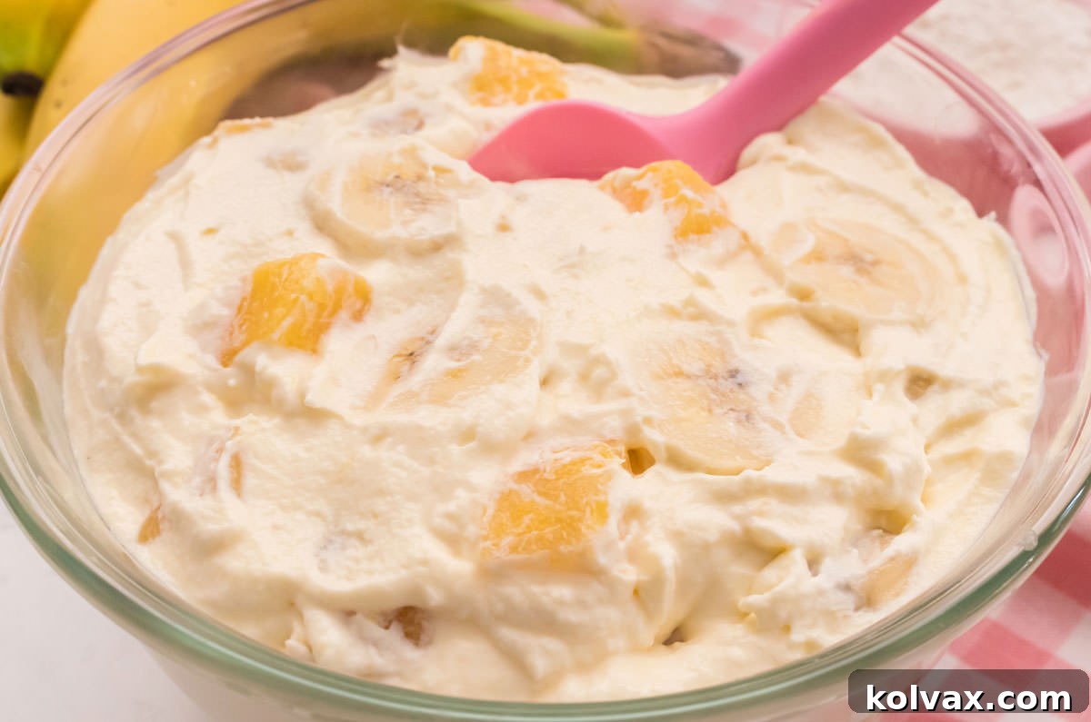 Close up on the top of a glass bowl filled with chilled Pineapple Banana Fluff sitting on a pink table linen. This light and fluffy dessert is bursting with banana and pineapple flavor, perfect for any gathering.