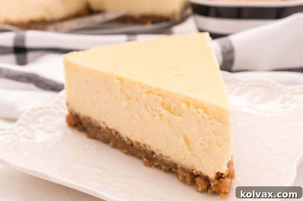 A closeup on a slice of classic cheesecake sitting on a white plate in front of a black and white table linen, showcasing its creamy texture and golden crust.