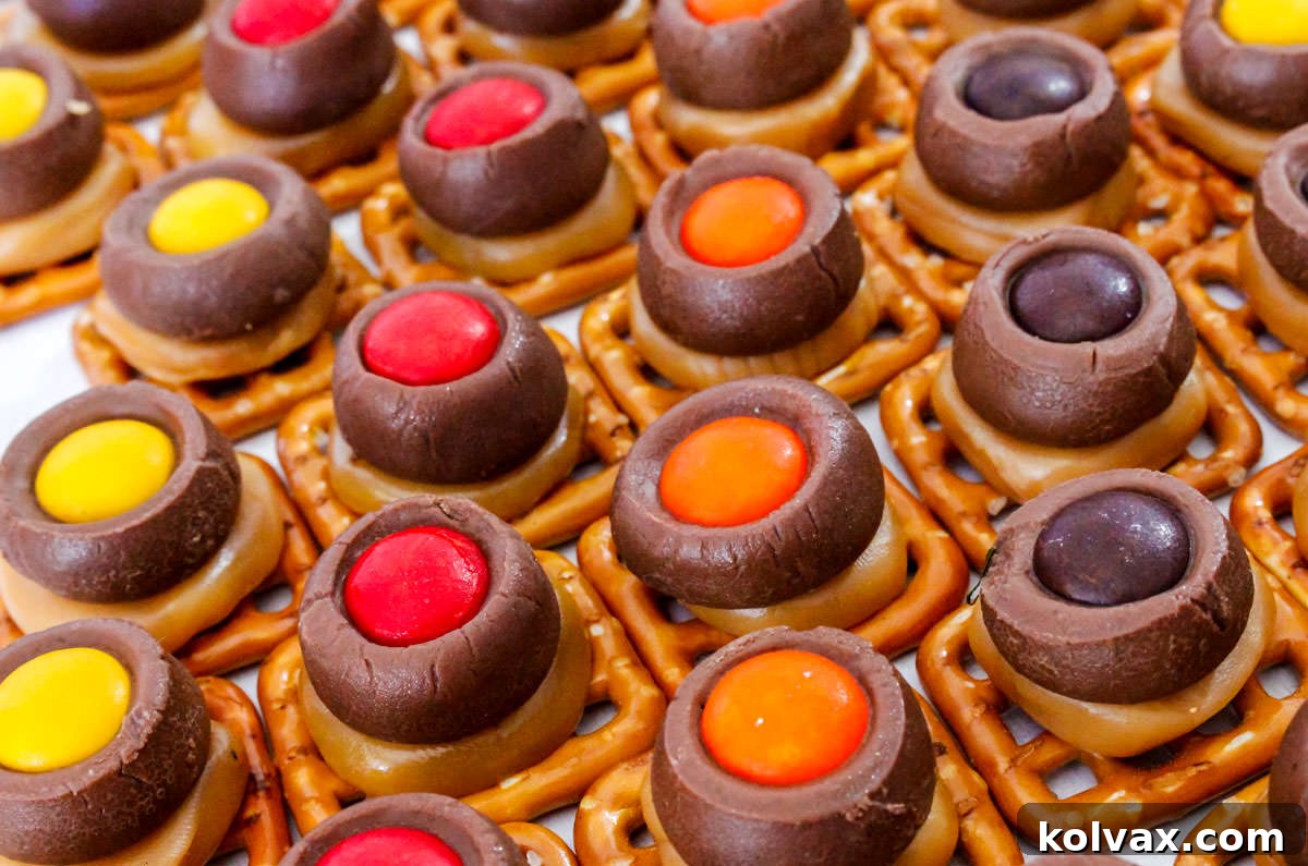 Closeup on rows of Thanksgiving Chocolate Caramel Pretzel Bites sitting on a white table, adorned with festive M&M's.