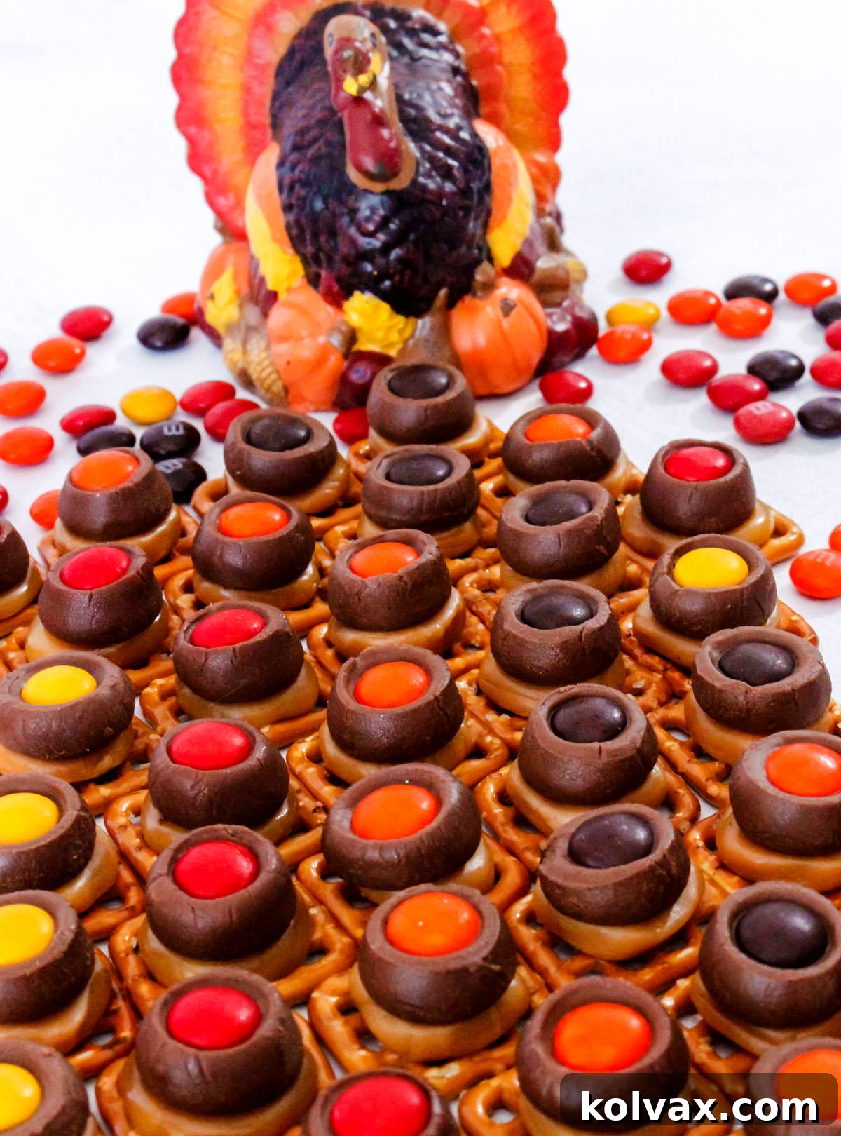 A batch of Thanksgiving Chocolate Caramel Pretzel Bites sitting on a white surface, with a festive turkey-shaped candle in the background, ready for holiday celebrations.