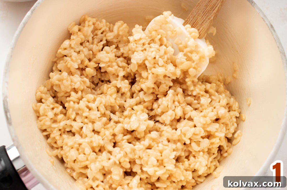 Autumn Foliage Rice Krispie Bars 4 A close-up of warm, melted Rice Krispie Treat mixture in a white saucepan, being stirred with a white wooden spoon, ready for coloring and cereal.