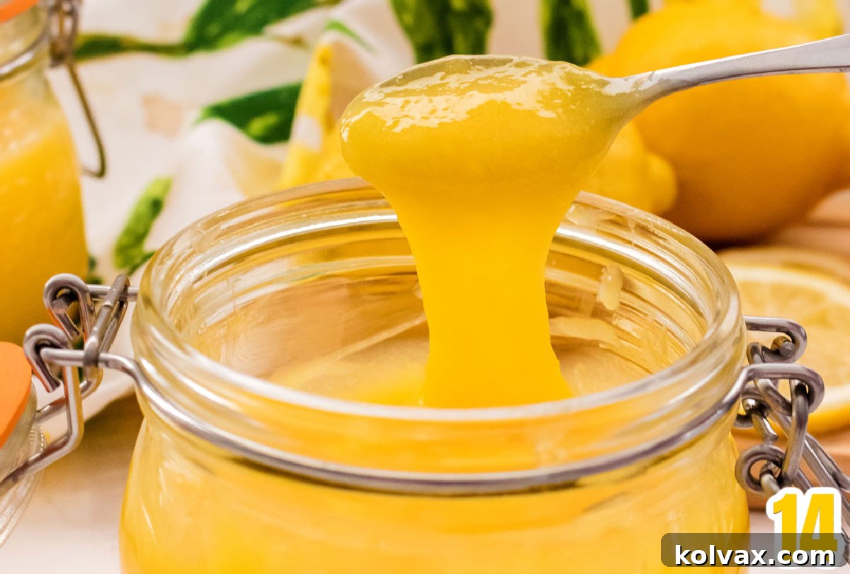 Close-up of a spoon filled with luscious homemade Lemon Curd, hovering over a glass jar brimming with the creamy spread, with fresh lemons in the background.