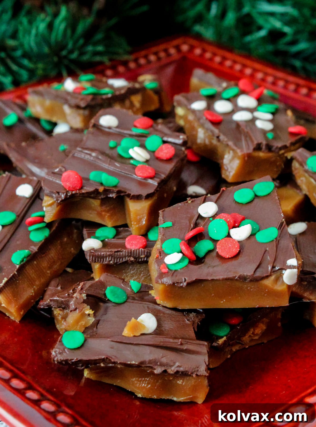 Closeup on a batch of Homemade English Toffee sitting on a red plate surrounded by Christmas decorations, ready to be served.