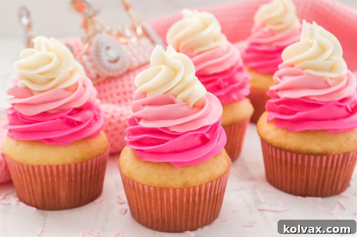 Five Pink Ombre Princess Cupcakes arranged beautifully on a white table, set against a backdrop of soft pink linen and a shimmering pink princess tiara. Each cupcake features a delicate swirl of pink and white buttercream frosting.