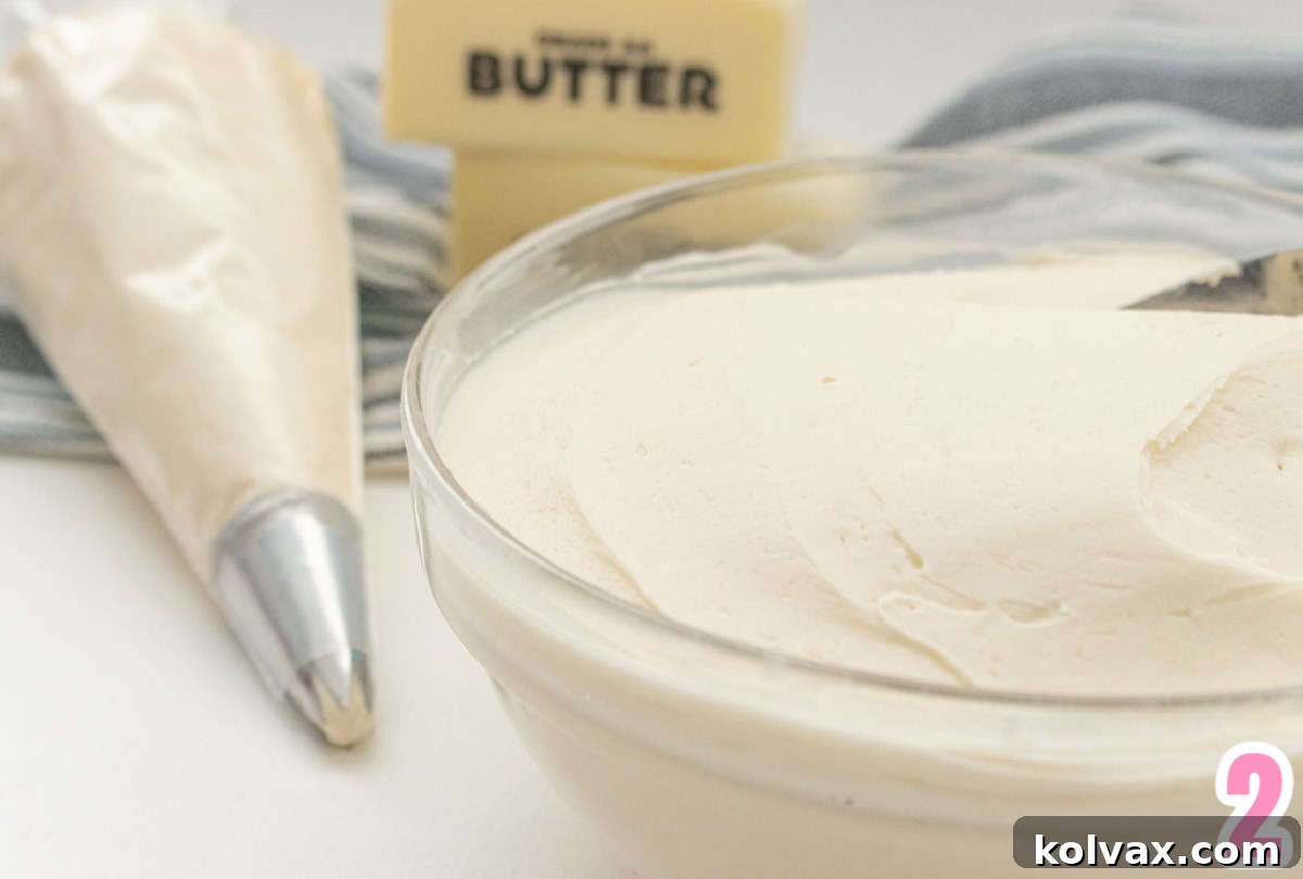 A glistening clear bowl of freshly made homemade buttercream frosting sits beside two sticks of softened butter, with a piping bag filled with the creamy white frosting ready for decoration. This image highlights the key component of Princess Cupcakes.
