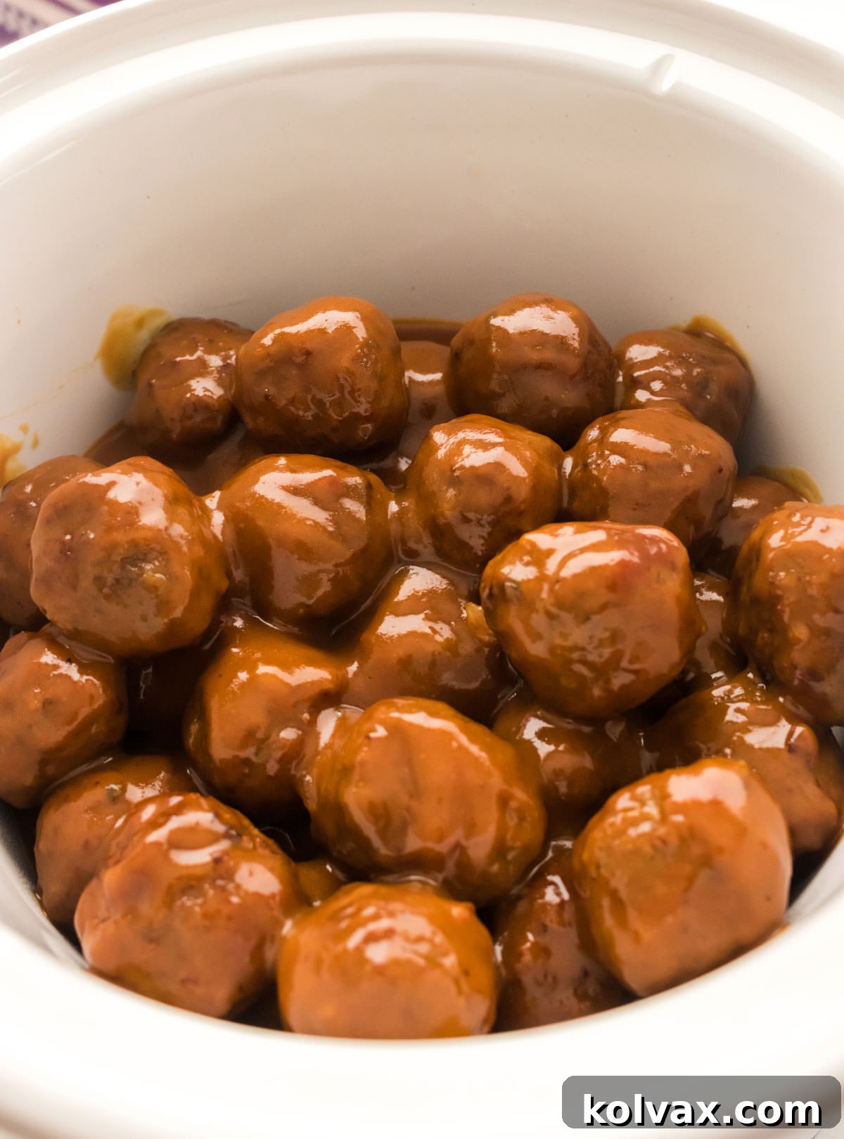 A top-down view of a white Crockpot brimming with perfectly cooked Grape Jelly Meatballs, simmering in their delicious, glossy sauce.