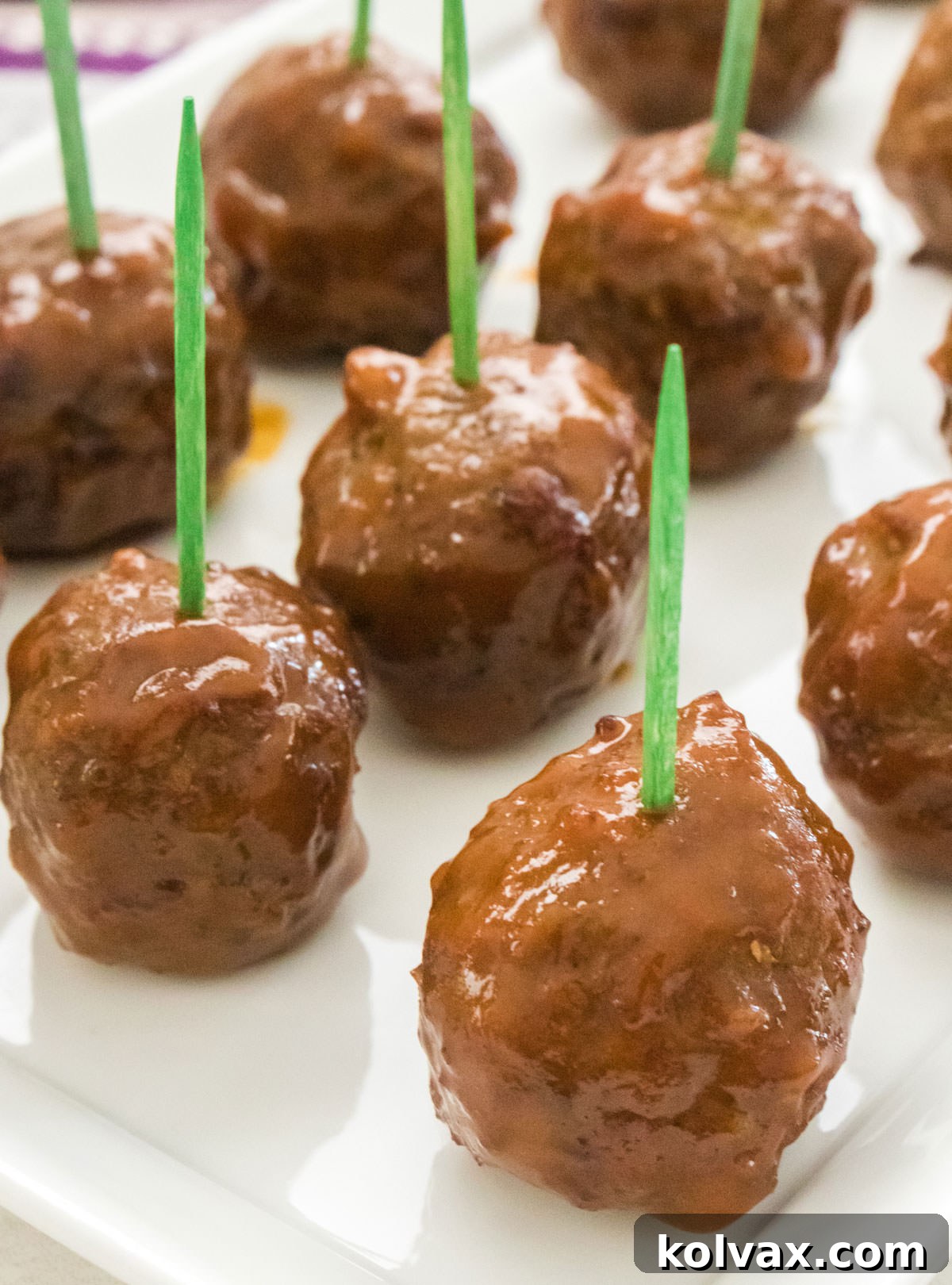 A pristine white serving platter filled with an abundance of glossy Grape Jelly Meatballs, each skewered with a toothpick, inviting guests to indulge.