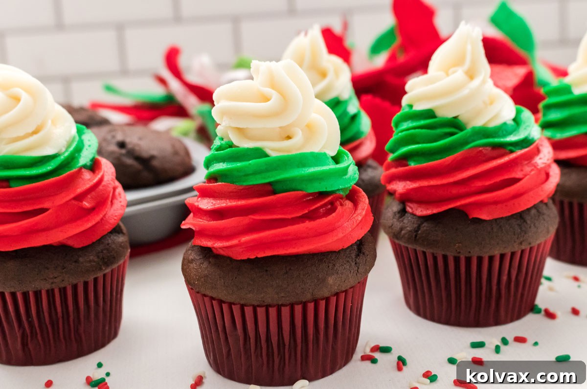 Closeup on five Easy Christmas Cupcakes sitting on a white table surrounded by Christmas sprinkles and Christmas decorations, showcasing their vibrant red, green, and white buttercream frosting swirl.