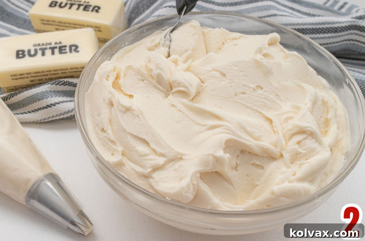 A clear glass bowl brimming with light, fluffy, homemade buttercream frosting, centered on a white table, ready to be colored and used.
