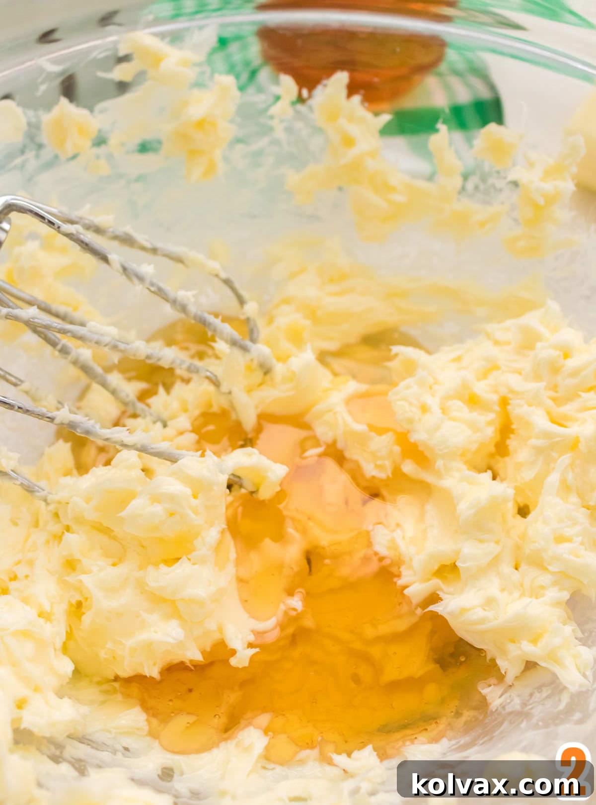 Closeup on a clear glass bowl filled with whipped butter, covered with honey and electric beaters.