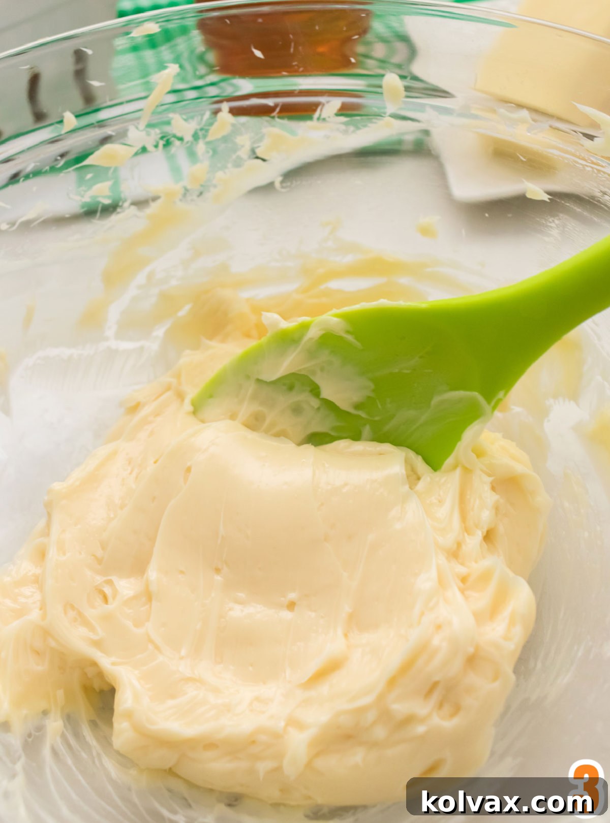 Closeup on a clear glass bowl filled with honey butter and a green spatula.