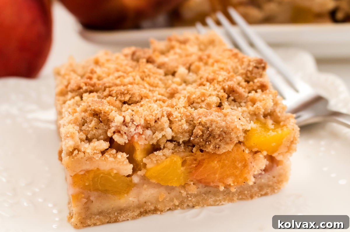 Closeup on a single Peach Crumble Bar on a white plate with a fork with peaches and more cookie bars in the background.