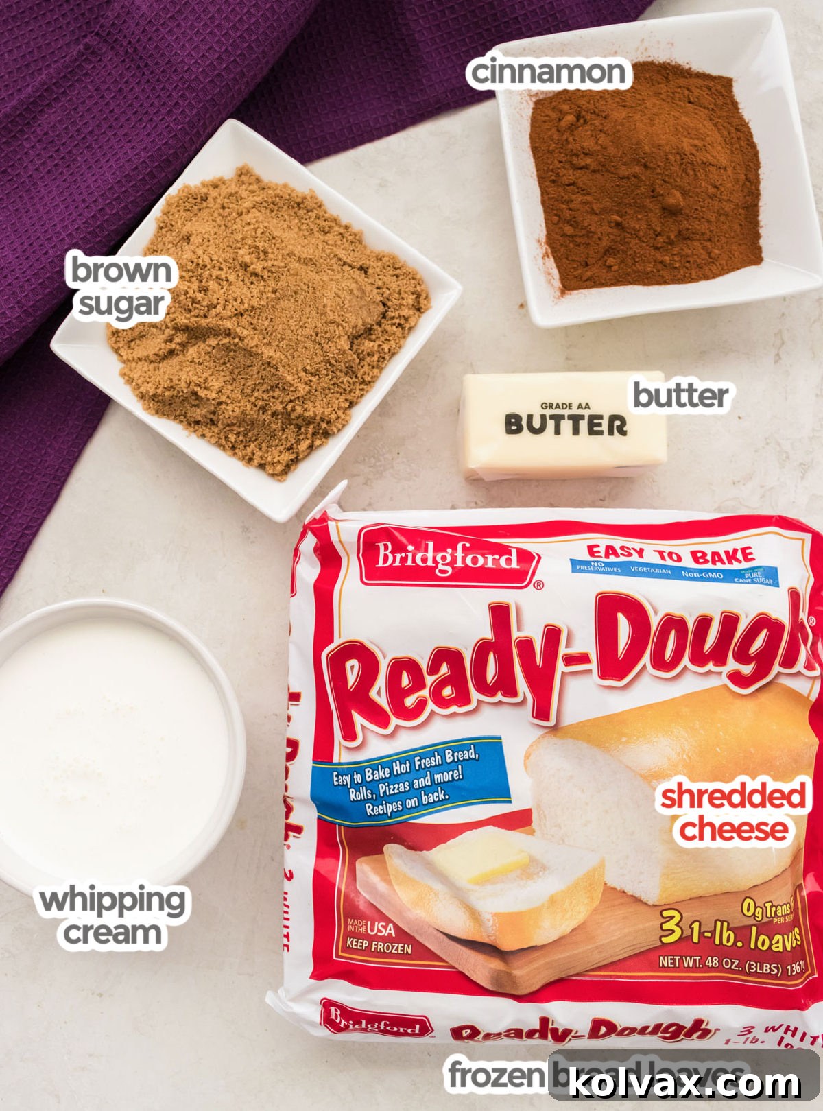 A flat lay photograph showcasing all the key ingredients required to bake Caramel Sticky Buns: a package of Bridgford Ready-Dough, sticks of butter, a carton of heavy whipping cream, a bowl of rich brown sugar, and ground cinnamon.