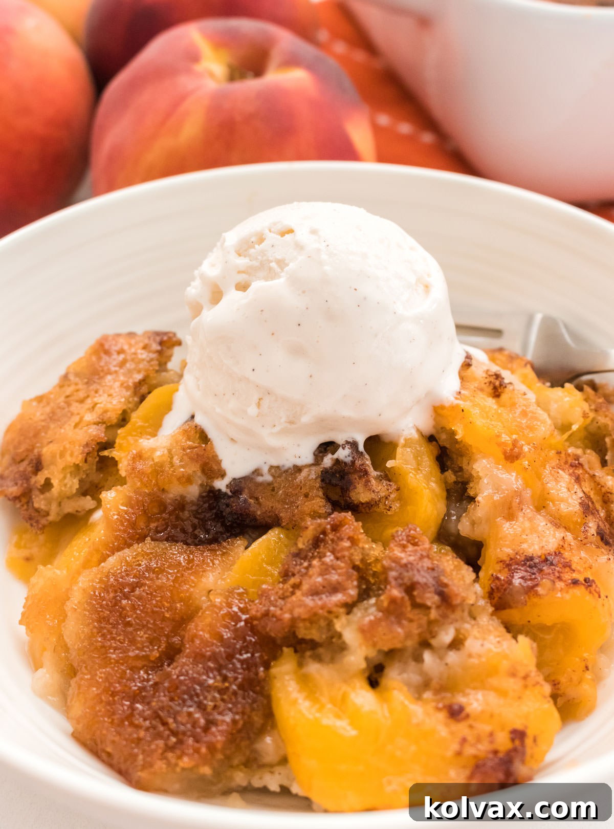 Heirloom Peach Cobbler 9 Closeup on a pristine white bowl generously filled with warm, golden-brown Old Fashioned Peach Cobbler, decadently topped with a large, melting scoop of vanilla ice cream, creating a perfect balance of warm and cold textures.