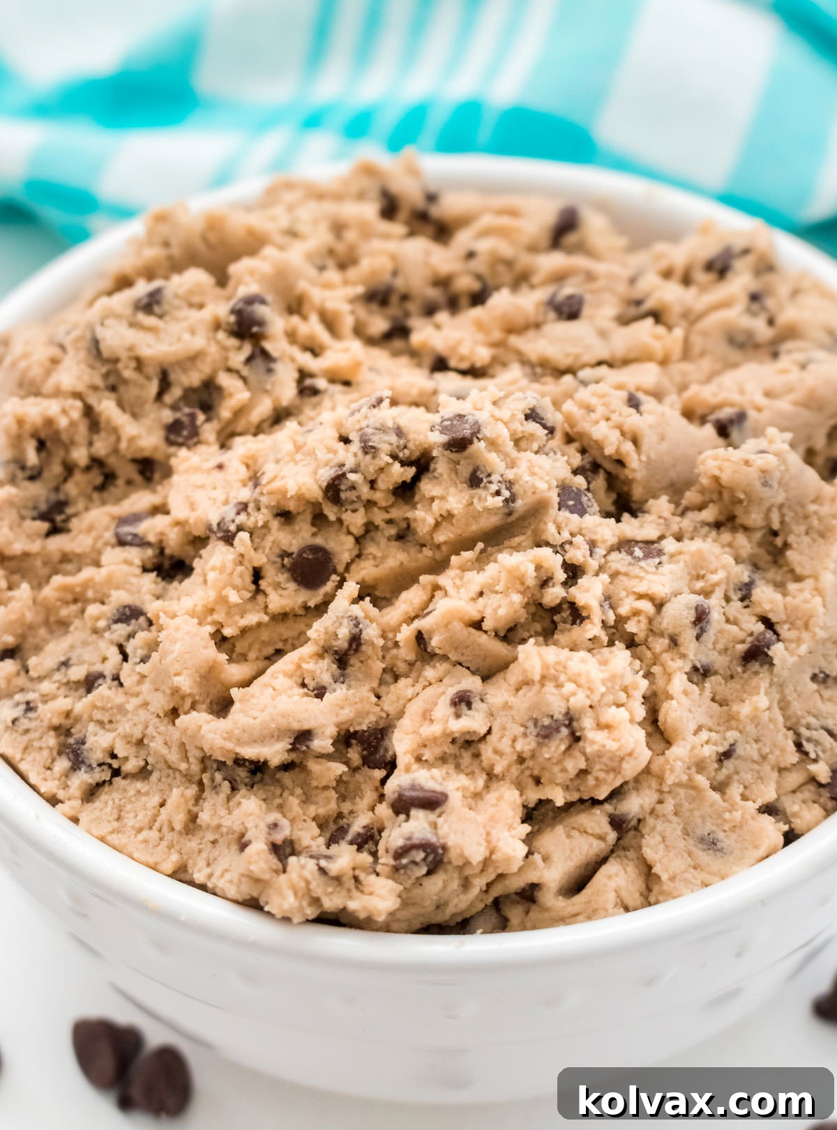Closeup on a white bowl filled with Edible Cookie Dough sitting on a white table in front of an aqua table linen, ready to be enjoyed.