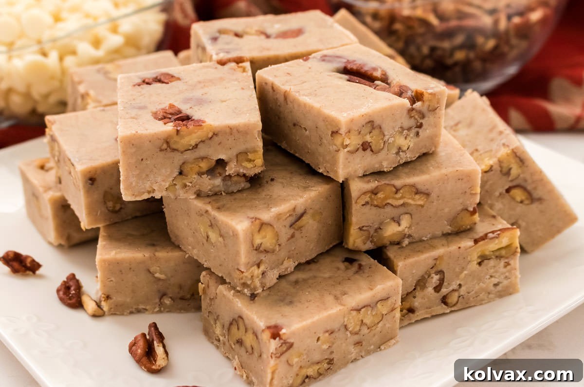 A stack of golden-brown Butter Pecan Fudge pieces on a white plate, with bowls of pecans and white chocolate chips in the background, highlighting the key ingredients.