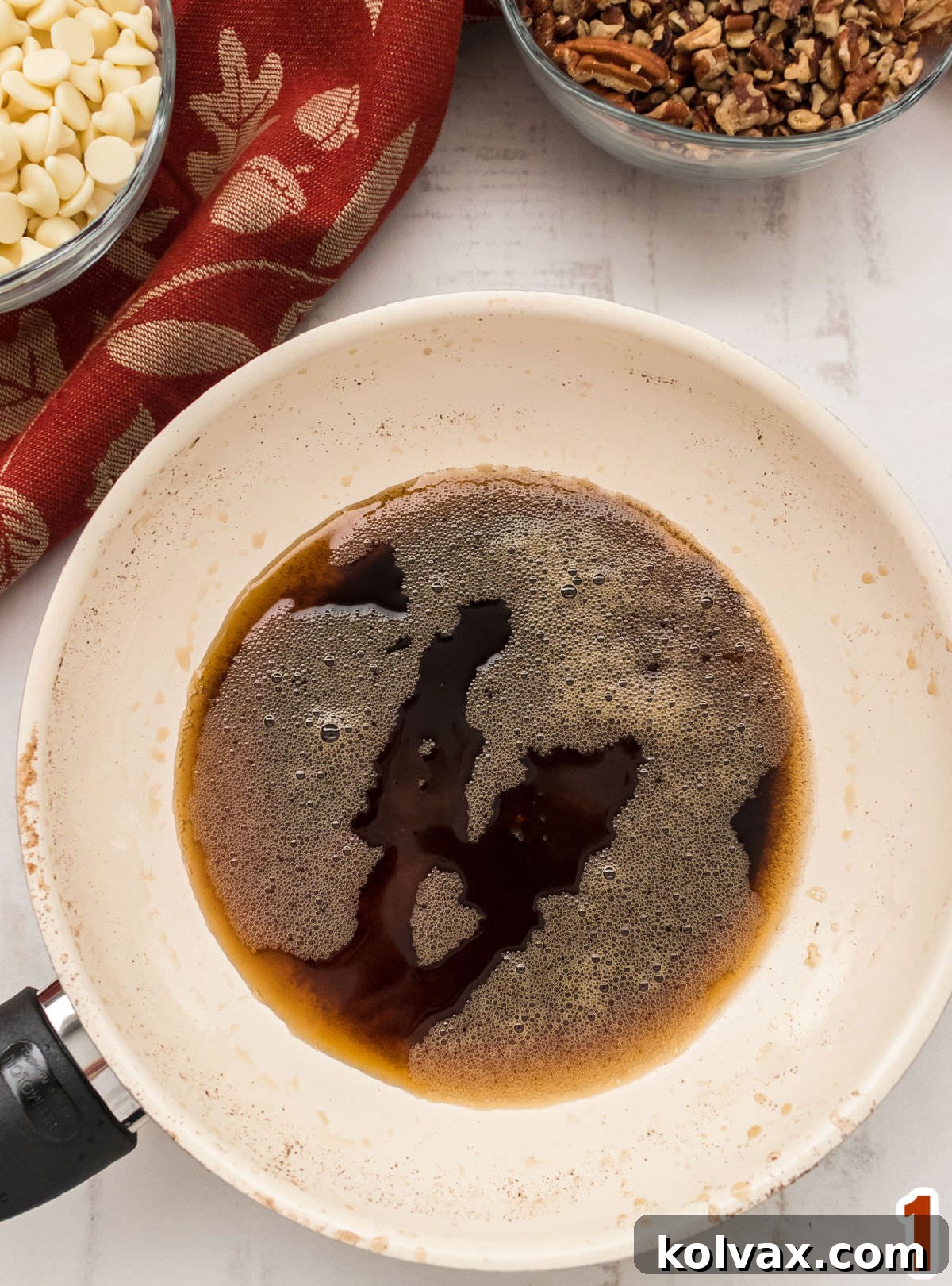 Close-up of a pan filled with beautifully browned butter, surrounded by pecans and white chocolate chips, showcasing the golden color and nutty bits.