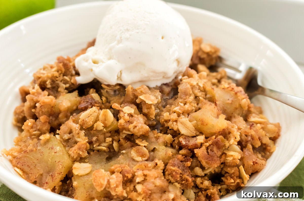 A close-up shot of a white bowl filled with Easy Apple Crisp, topped with a generous scoop of melting vanilla ice cream, resting on a cozy green kitchen towel.